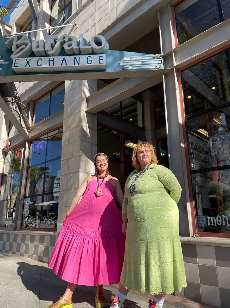 Two people standing in front of shop windows wearing solid pink and green midi dresses