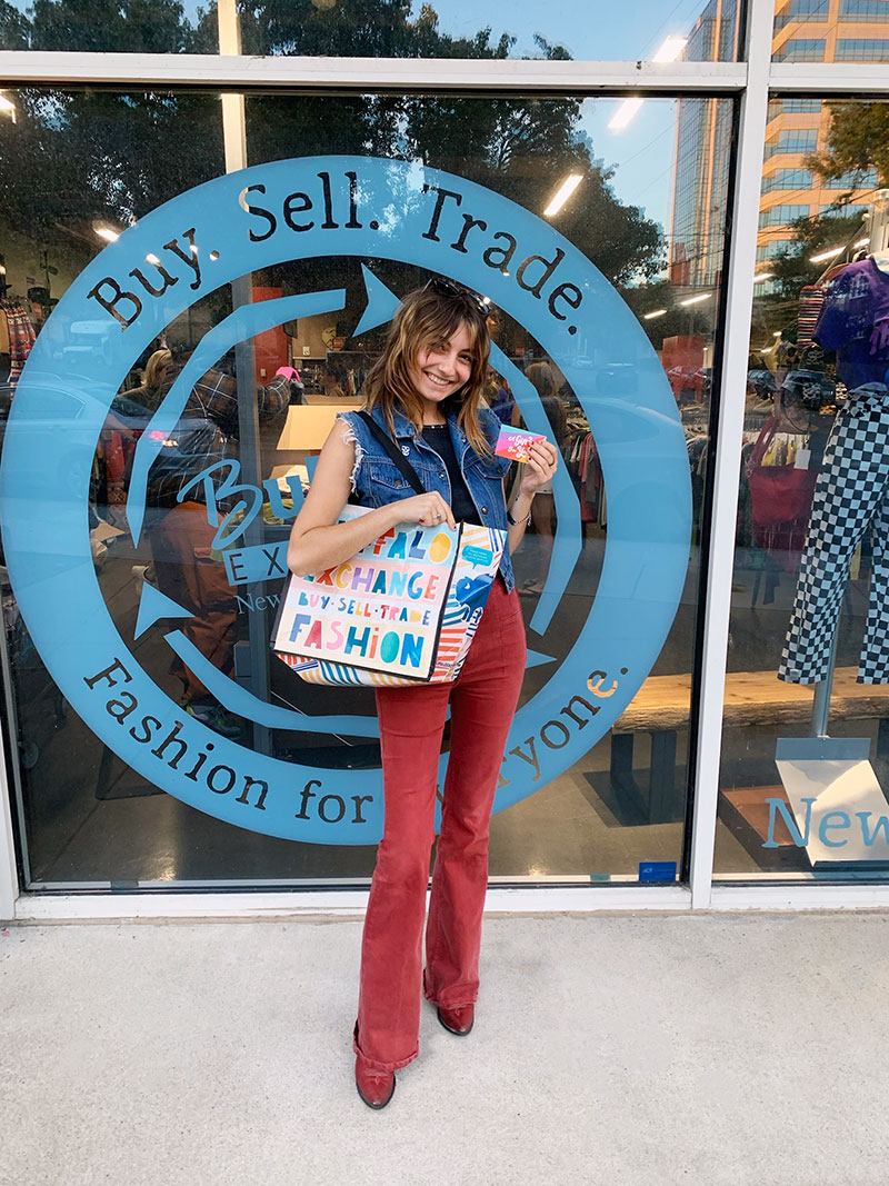 A person stands in front of the window at Buffalo Exchange Nashville with a Buffalo Exchange tote on their shoulder and trade card in-hand