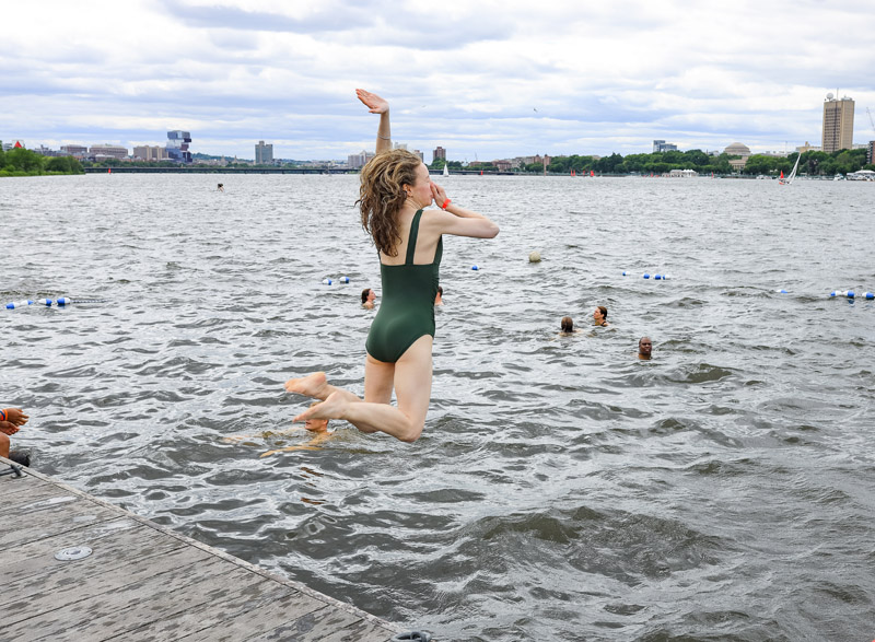 Person wearing green swimsuit jumping into the Charles River.