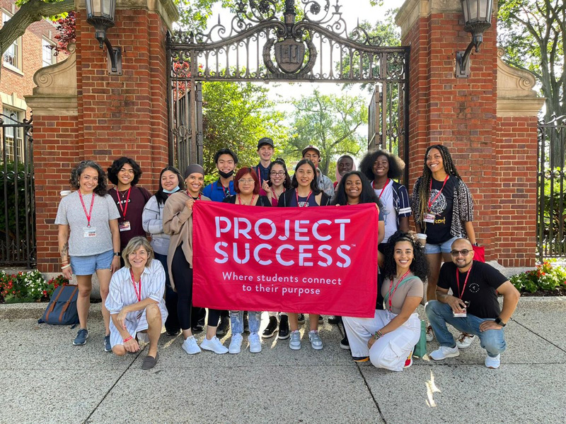 Group of people holding a red Project Success banner in front of a brick archway.