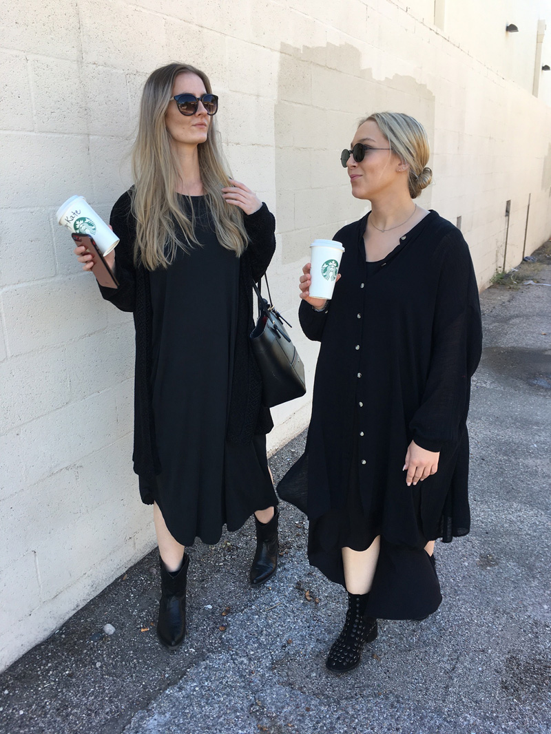 Two people recreating a paparazzi photo of Mary Kate and Ashley, both wearing all black dresses, boots, sunglasses, and holding Starbucks.