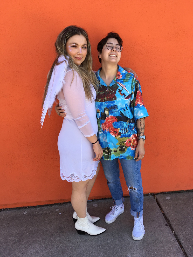 Two people wearing costumes from the movie Romeo + Juliet (1996), one person is wearing a white dress with angel wings and the other a Hawaiian button down shirt and jeans.
