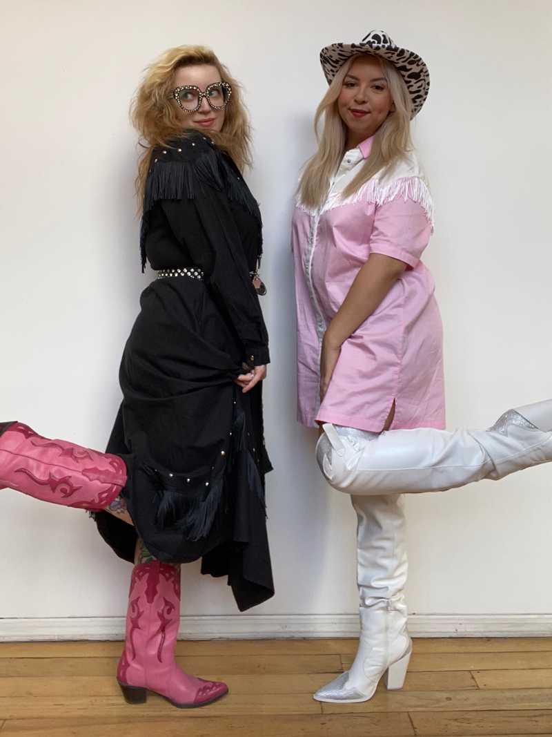 Two people wearing pink and black cowboy costumes with fringe, cowboy hats, and cowboy boots