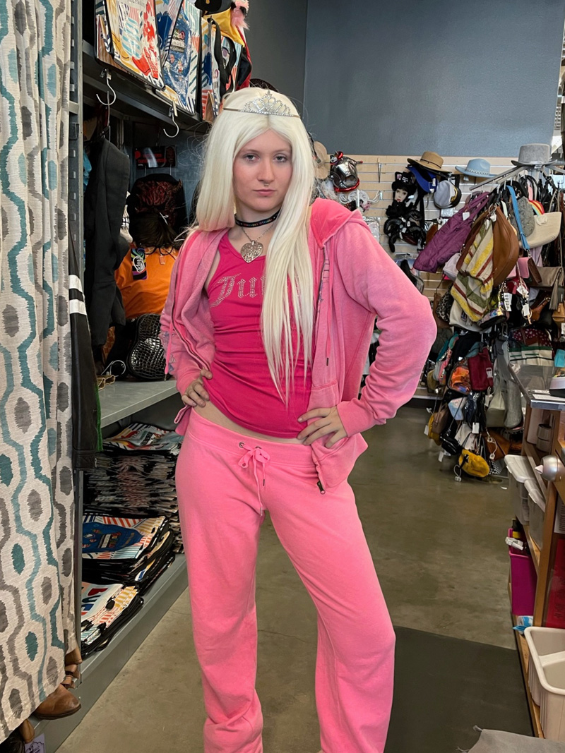 A person dressed as Paris Hilton wearing a tiara, a long, platinum blonde wig, a pink two-piece velour tracksuit, a hot pink rhinestone-bedazzled tank top, and pink shearling boots.