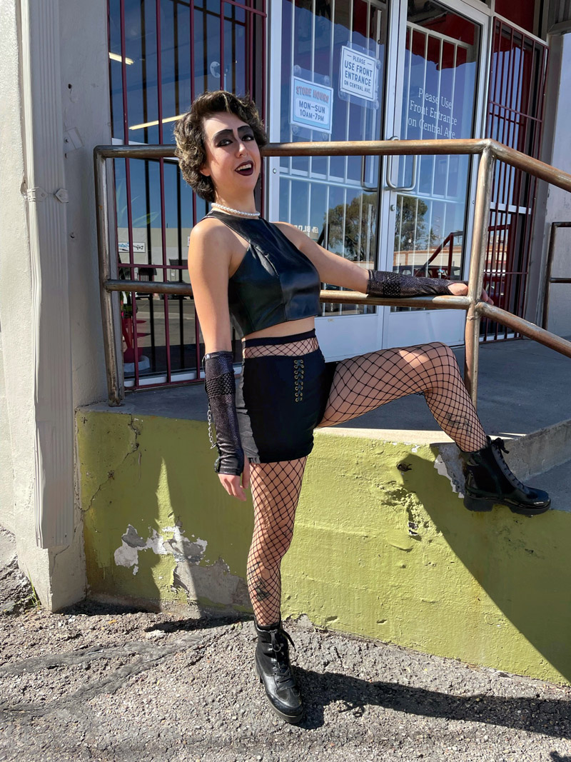 A person dressed as Frank-N-Furter with a theatrical eyeshadow look, and a black tank top, hot pants, fishnets, and arm sleeves.