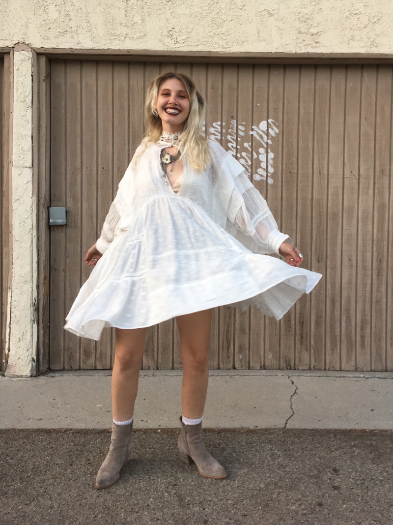 A person dressed as Stevie Nicks in a flowy white dress, suede booties, and layered bohemian necklaces.