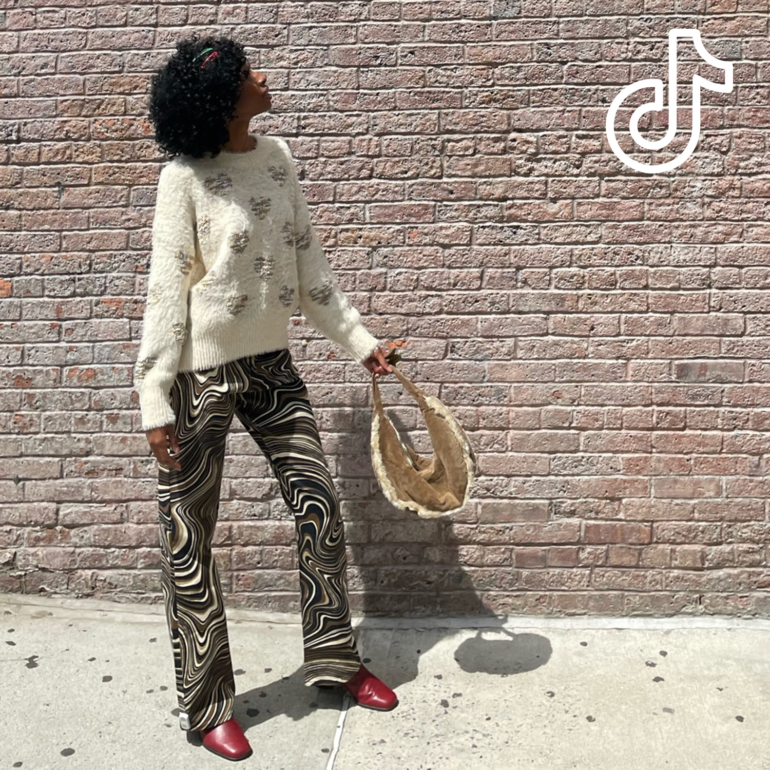 Woman wearing a fluffy white sweater paired with swirl pants, purse, and red leather shoes. [TikTok logo]