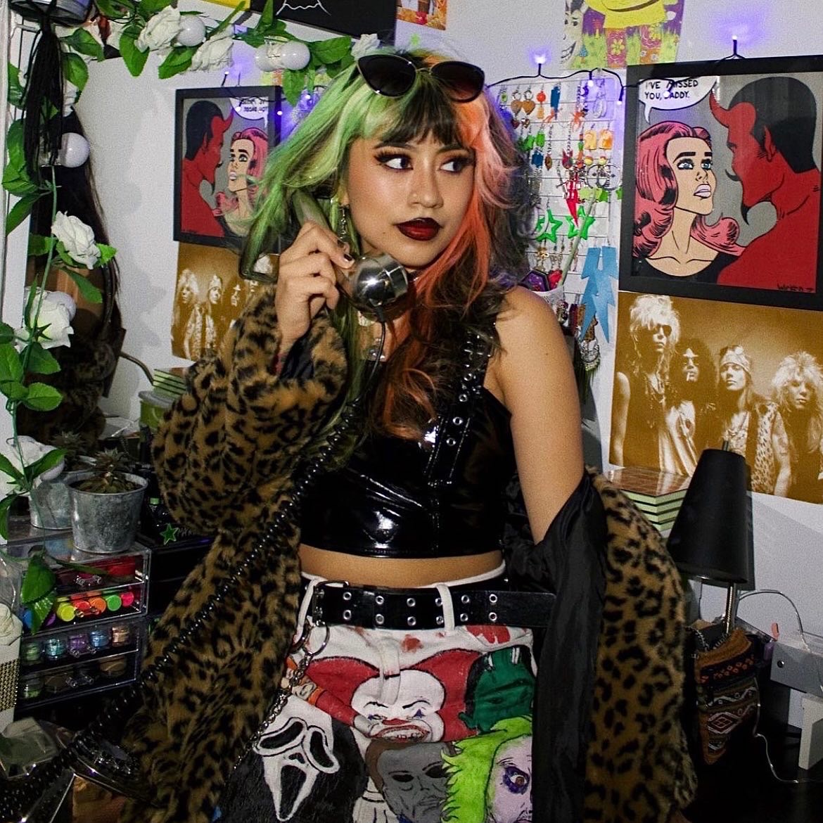 Girl with multicolored hair posing holding a corded phone and wearing a leopard print jacket and horror movie character skirt