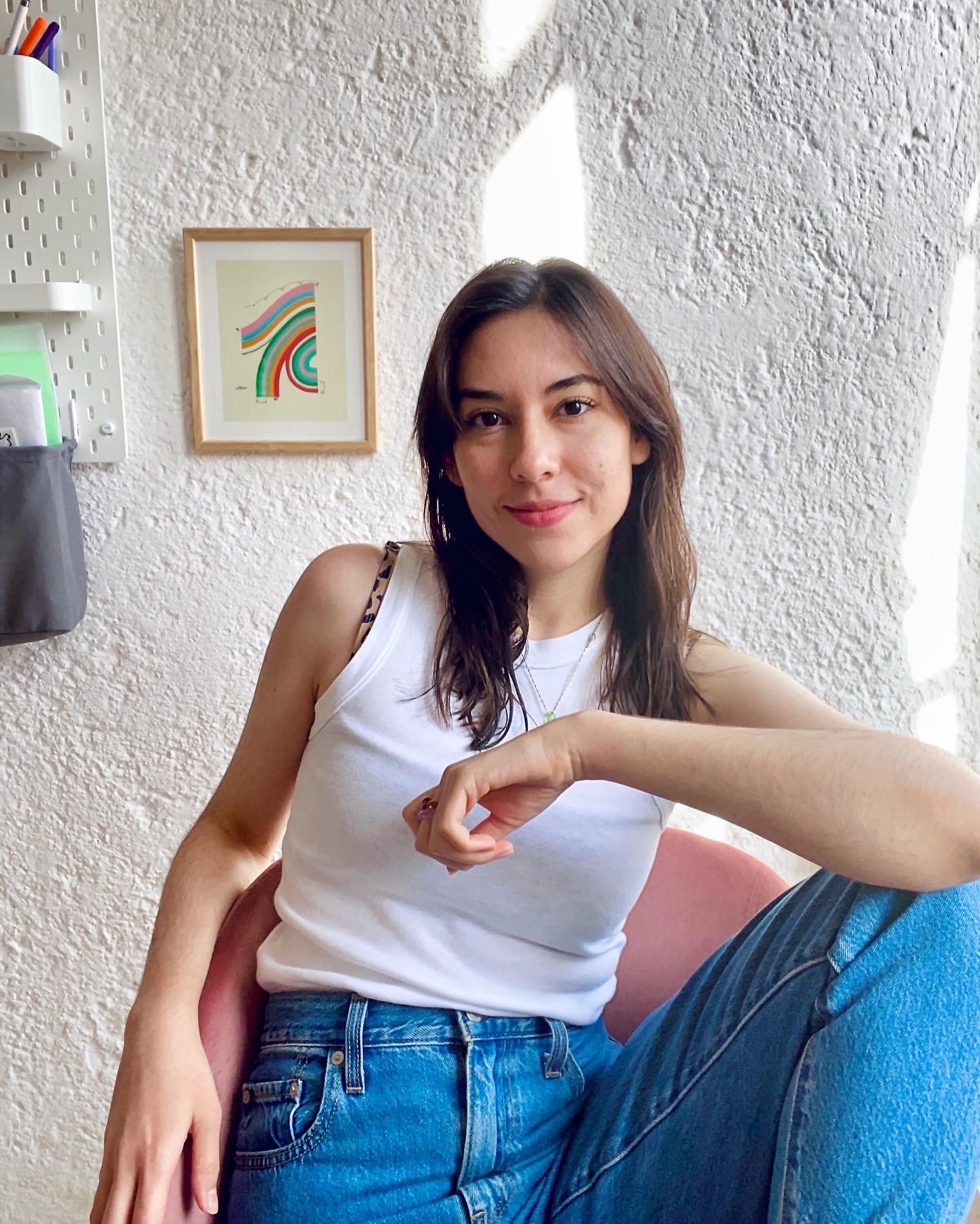 girl posing on a chair with her elbow on her knee, she is wearing blue jeans and a white tank top