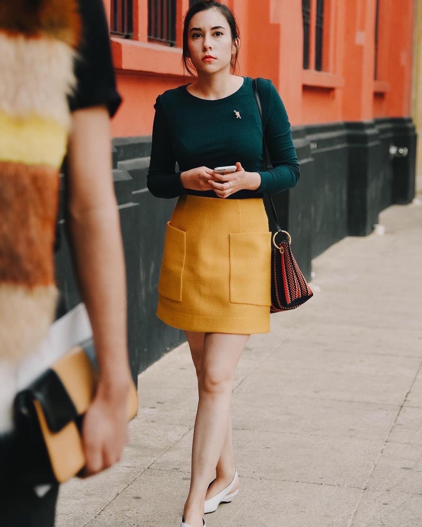 girl walking on a sidewalk wearing a yellow mini skirt and a dark green sweater