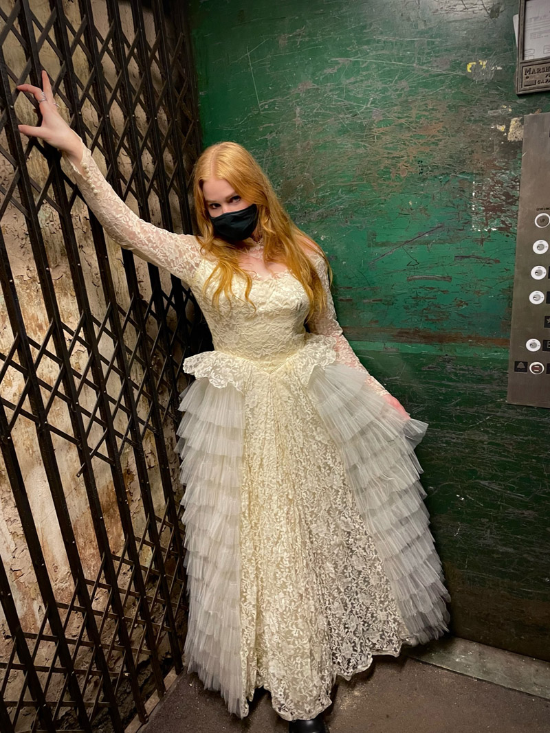 A person wearing a cream colored vintage lace and tulle ball gown.