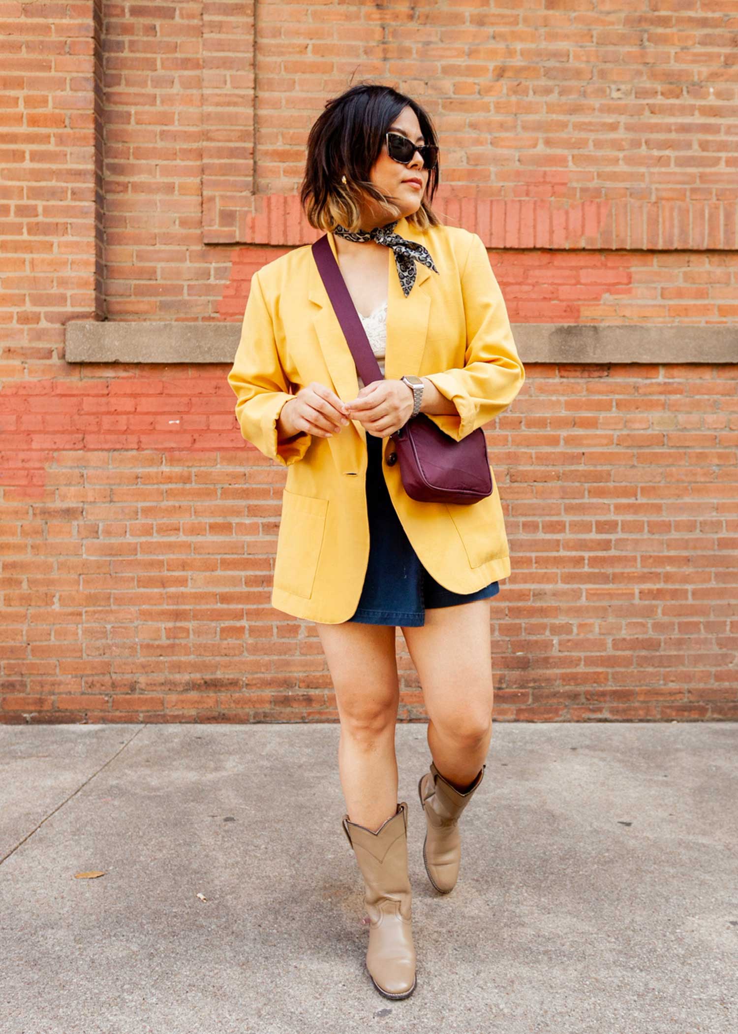 Girl posing in front of a brick wall wearing shorts and an oversized yellow blazer