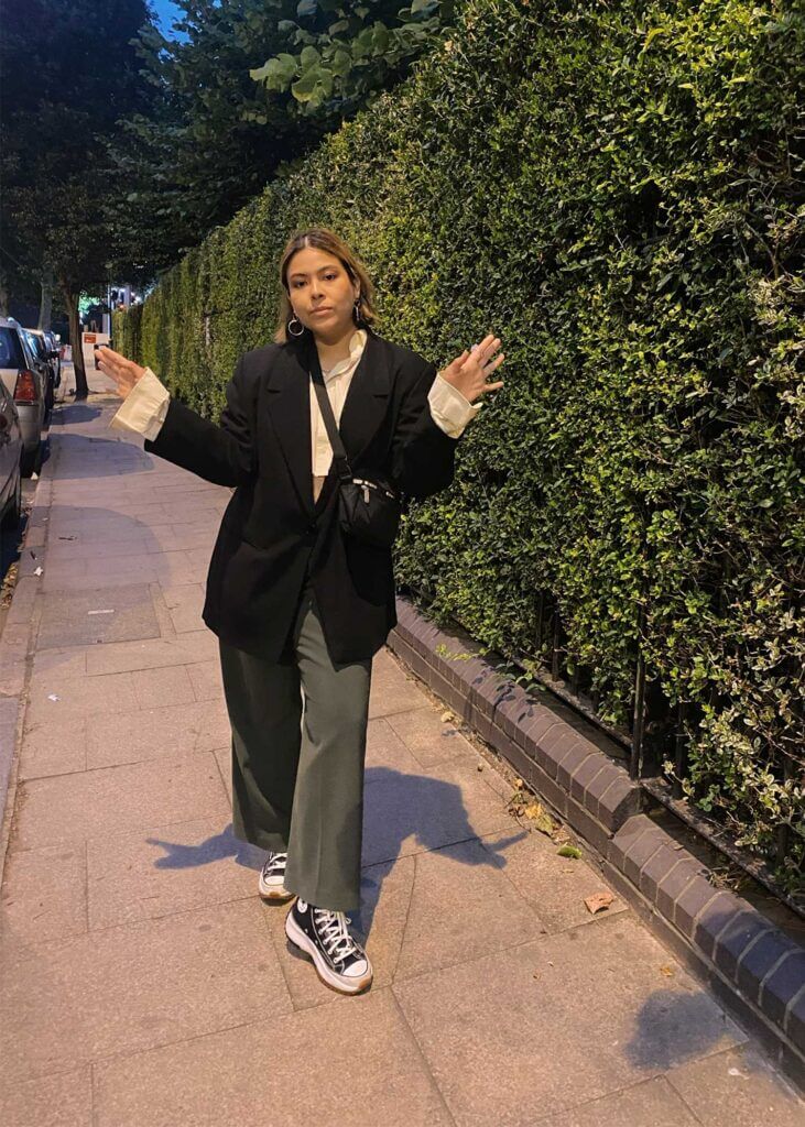 girl posing by a garden wall wearing a black oversized blazer and wide leg pants