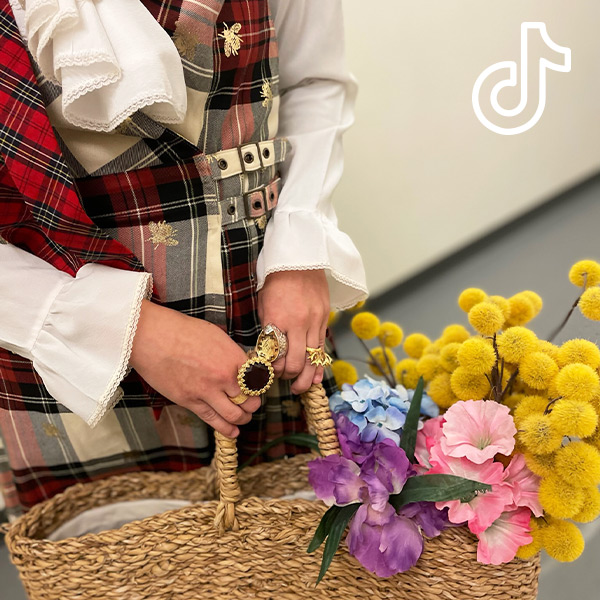Close up of a person in a Gucci outfit holding a raffia bag filled with flowers. [TikTok logo]