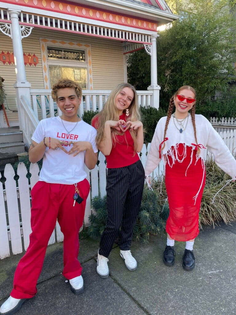 Three people wearing red and white clothes making heart symbols with their hands.