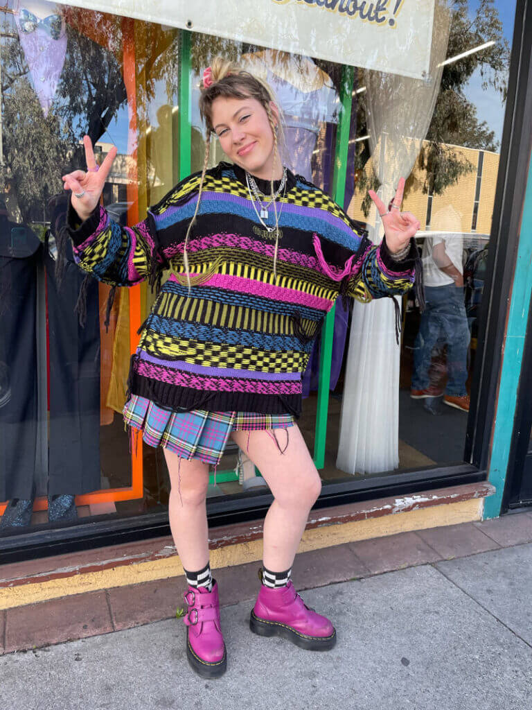 Person wearing striped and checkered mixed-print sweater and plaid mini skirt with pink boots.
