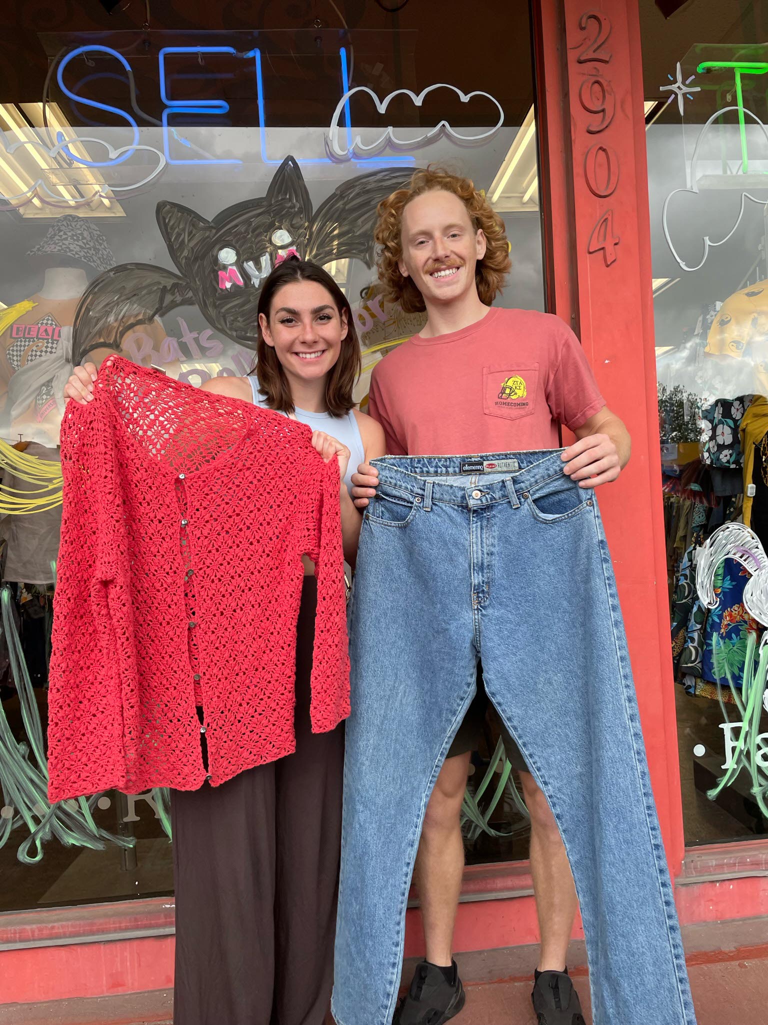 Two people holding clothes they found at the Earth Day $1 Sale 2022