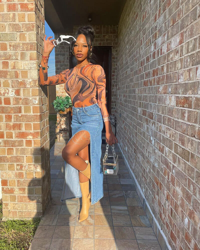 Customer @iam.pietty wearing a brown mesh marble-printed top, denim maxi skirt with a side slit and rhinestone detailing, and caramel pointed-toe boots.
