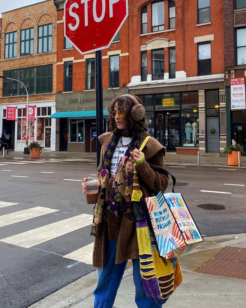 Customer @triniti.isaida wearing a brown waffle coat, cobalt blue pants, brown ear muffs, and a Buffalo Exchange recycled tote bag,