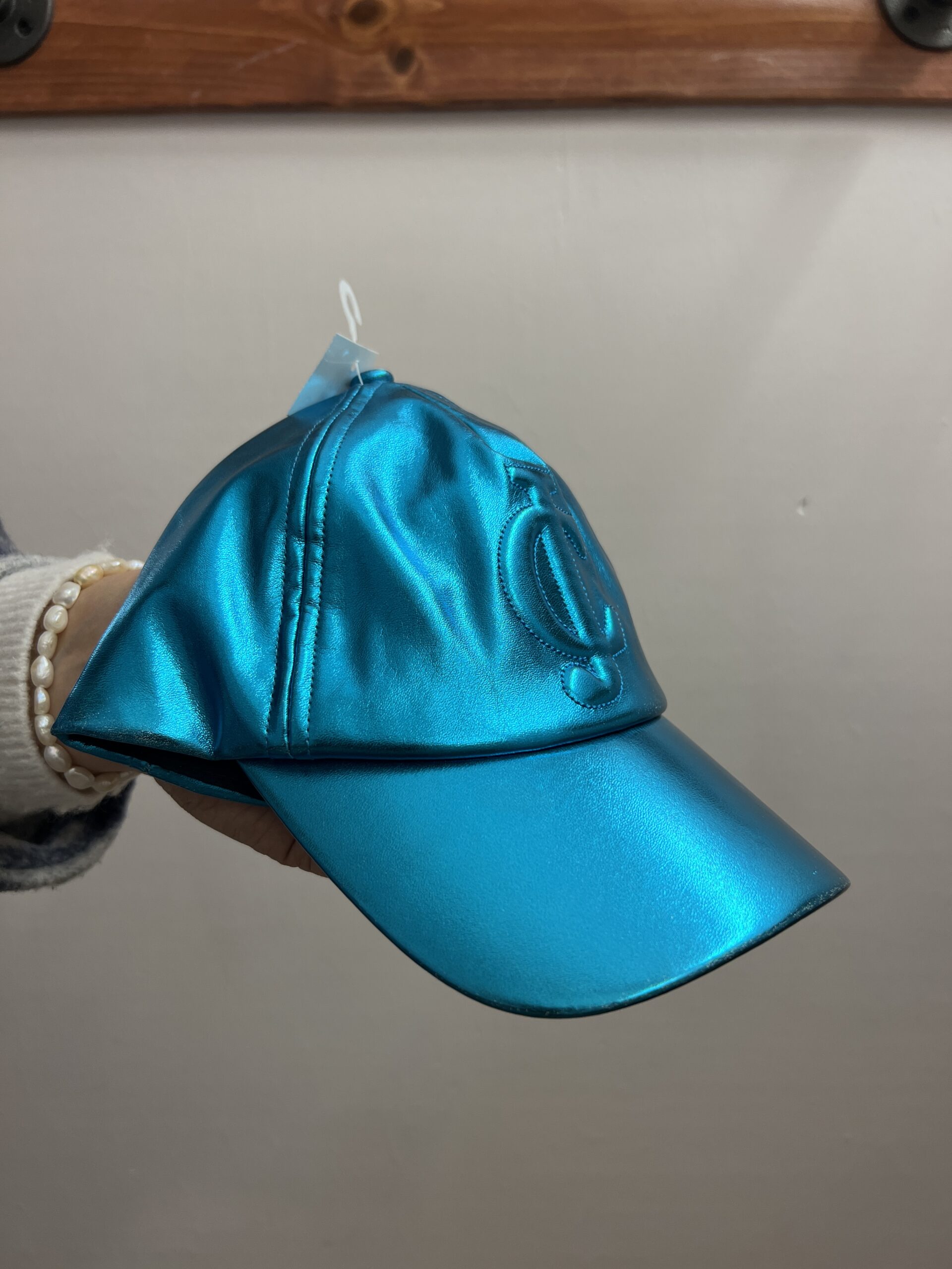 close up of a hand holding a Juicy Couture metallic blue baseball cap