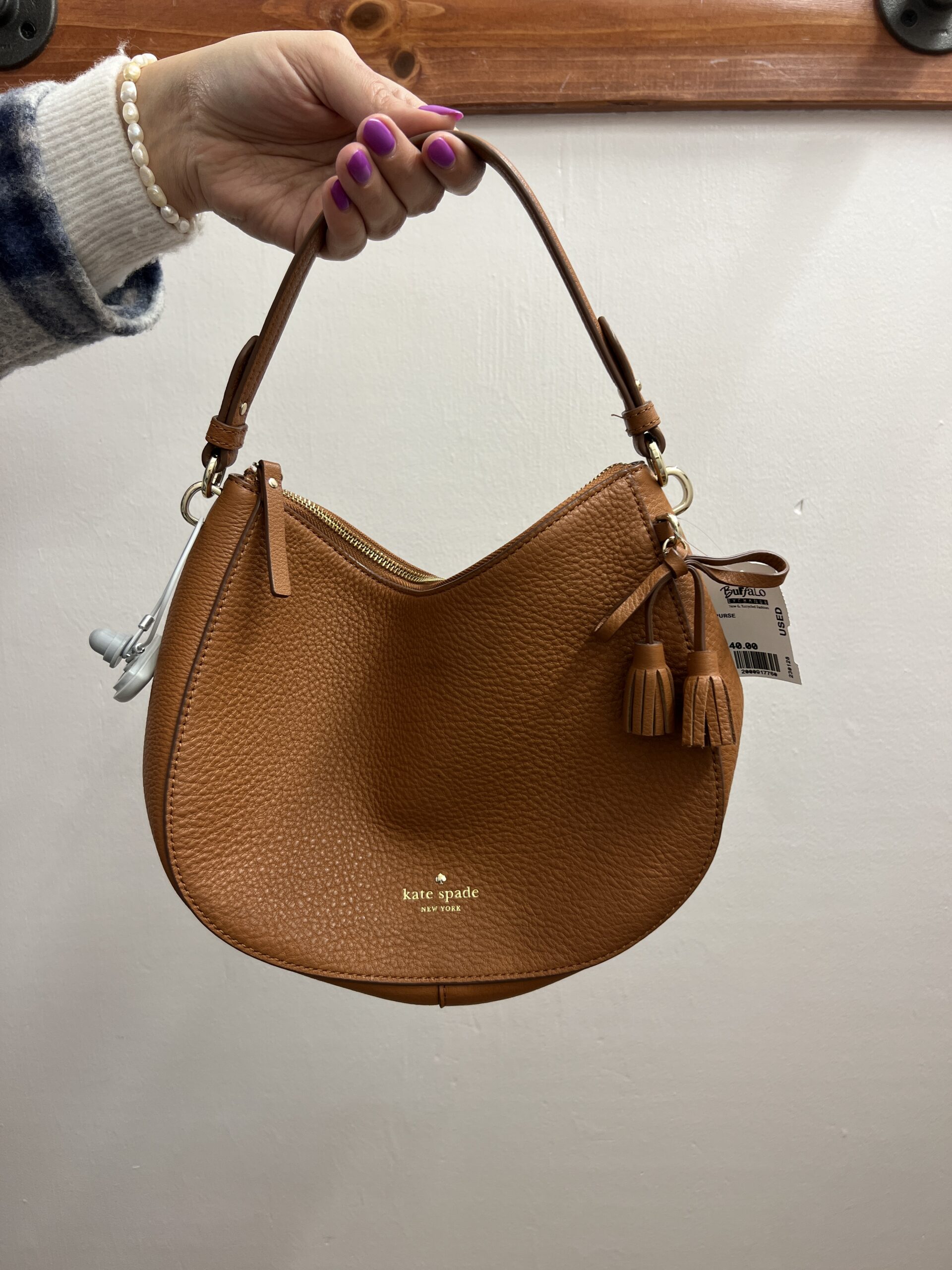 Close up of a hand holding a brown leather Kate Spade shoulder bag
