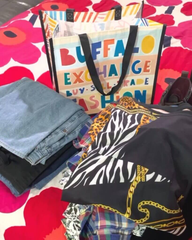 Clothes folded and one Buffalo Exchange Tote on top of a bed