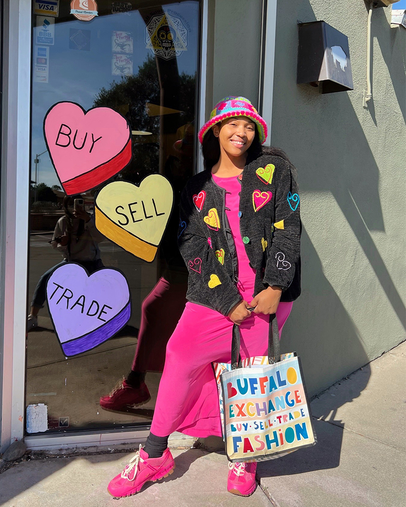 Person holding Buffalo Exchange tote bag standing in front of window painted with "Buy Sell Trade" conversation hearts 