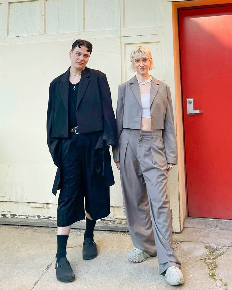 Two people wearing monochrome, oversized suits with cropped jackets