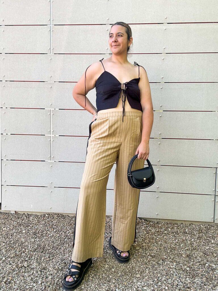 A woman wearing striped trousers and a dainty black tank top paired with black sandals and a black purse