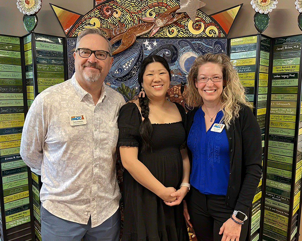 Group photo of three smiling people in front of tiled mosaic backdrop