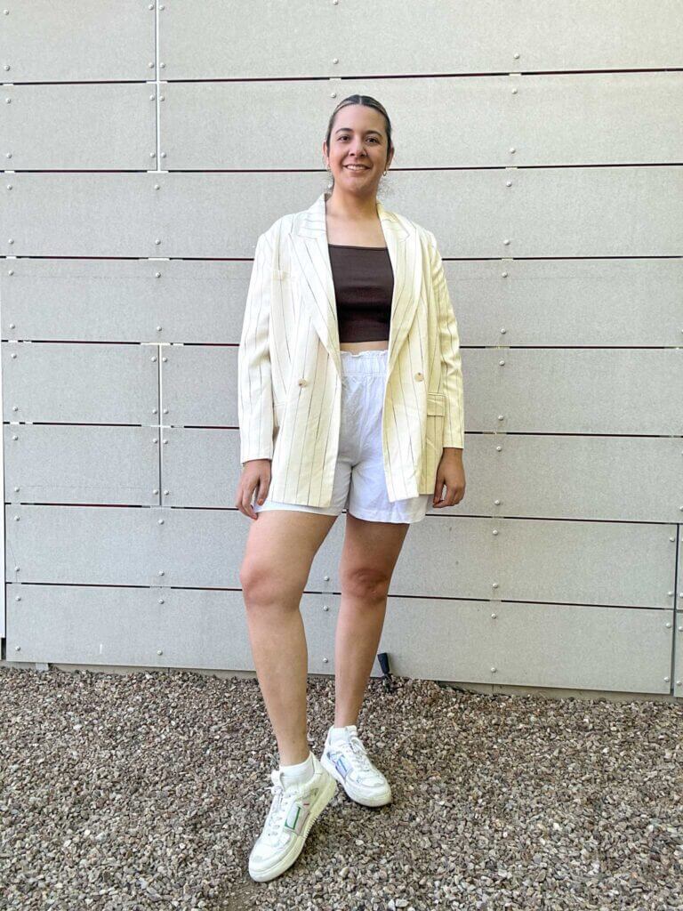 A woman wearing linen shorts, a tank top and a blazer paired with sneakers