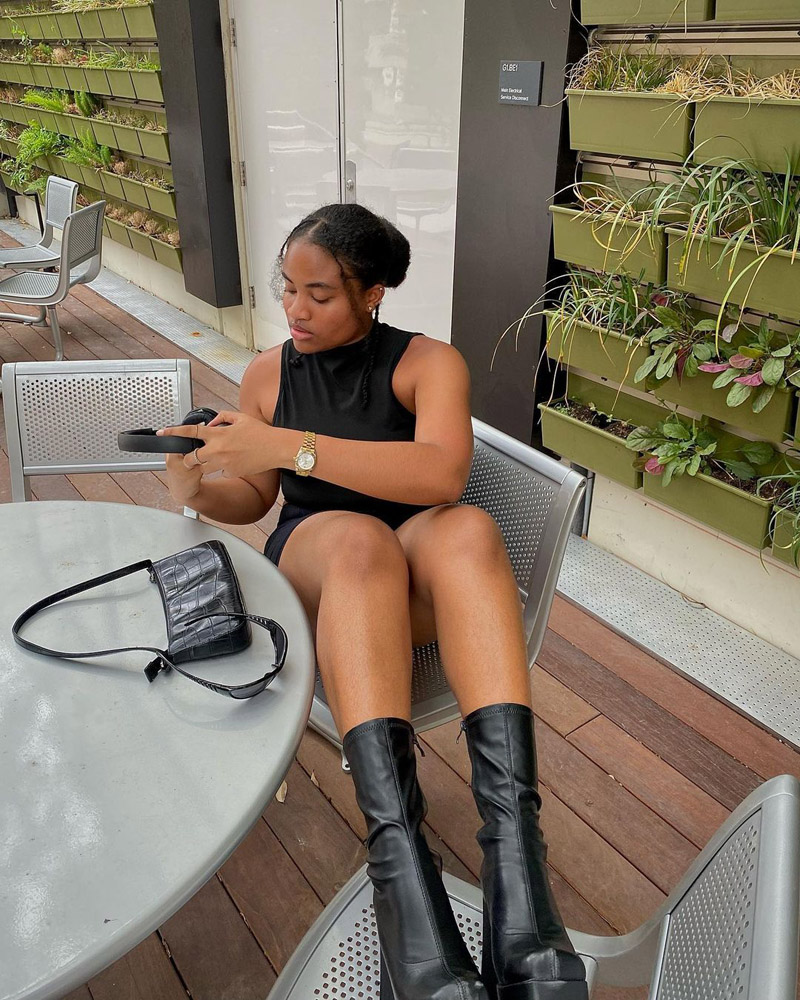 Customer @dianeaudrey.ak wearing a black dress, chunky ankle boots, a leather croc-effect shoulder bag, and a gold watch.