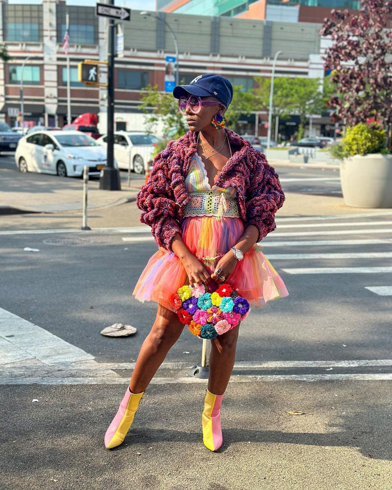 @theemodernhousewifeny wearing a chunky purple cardigan and a rainbow crochet tank top, tulle skirt, and patchwork handbag