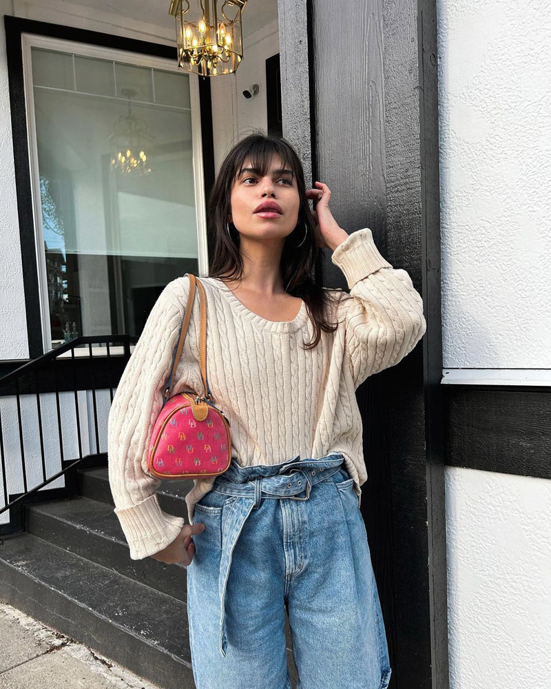 Customer @wilderfleur wearing a cream cable knit sweater tucked into paperbag-waist jeans, and a hot pink Dooney & Bourke shoulder bag
