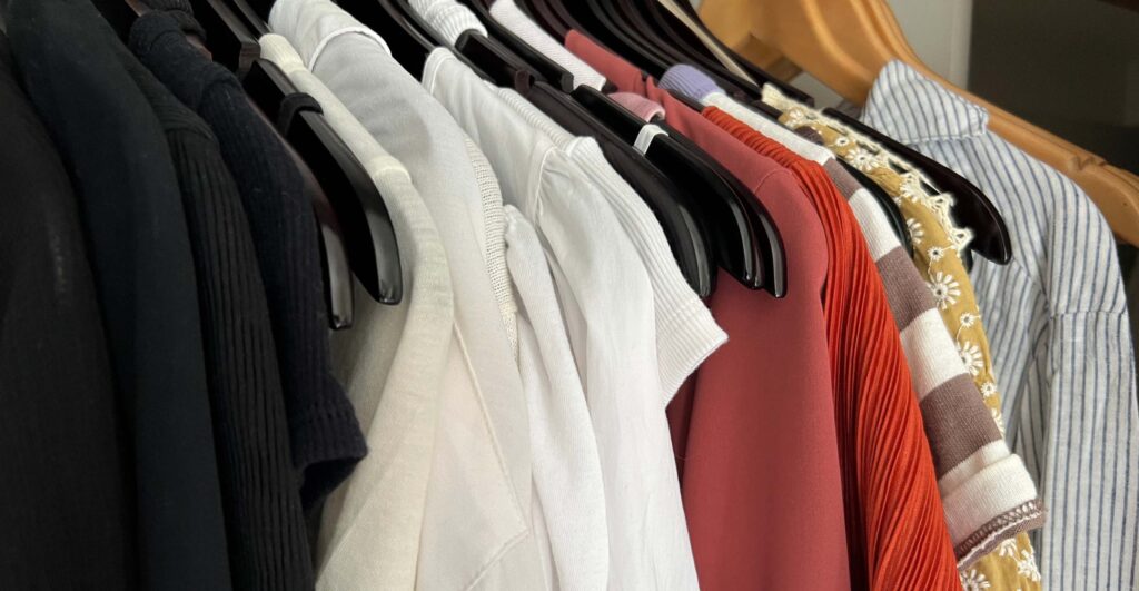 A close up photo of clothes hanging in a closet, roughly in order by color