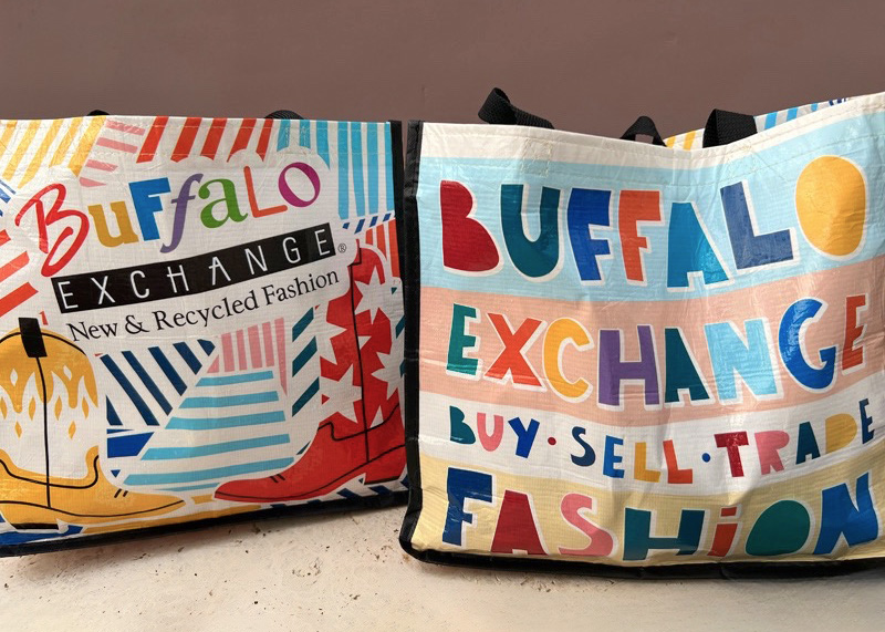 Two Buffalo Exchange tote bags filled with clothes ready to sell.