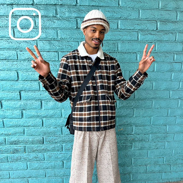 Person making peace signs wearing plaid jacket, twill pants and beanie