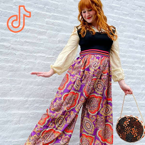 Person wearing 70s paisley flowy pants with cropped sweater vest and round bag