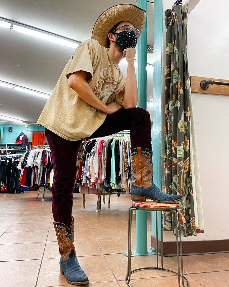 Person wearing cowboy hat, tee shirt, jeans and western boots poses on stool