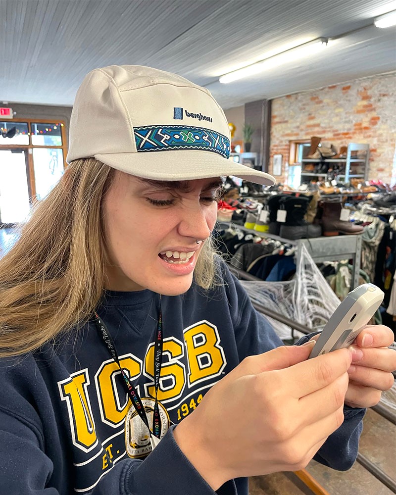 Person wearing baseball cap and UCSB sweatshirt squints at retro cellphone