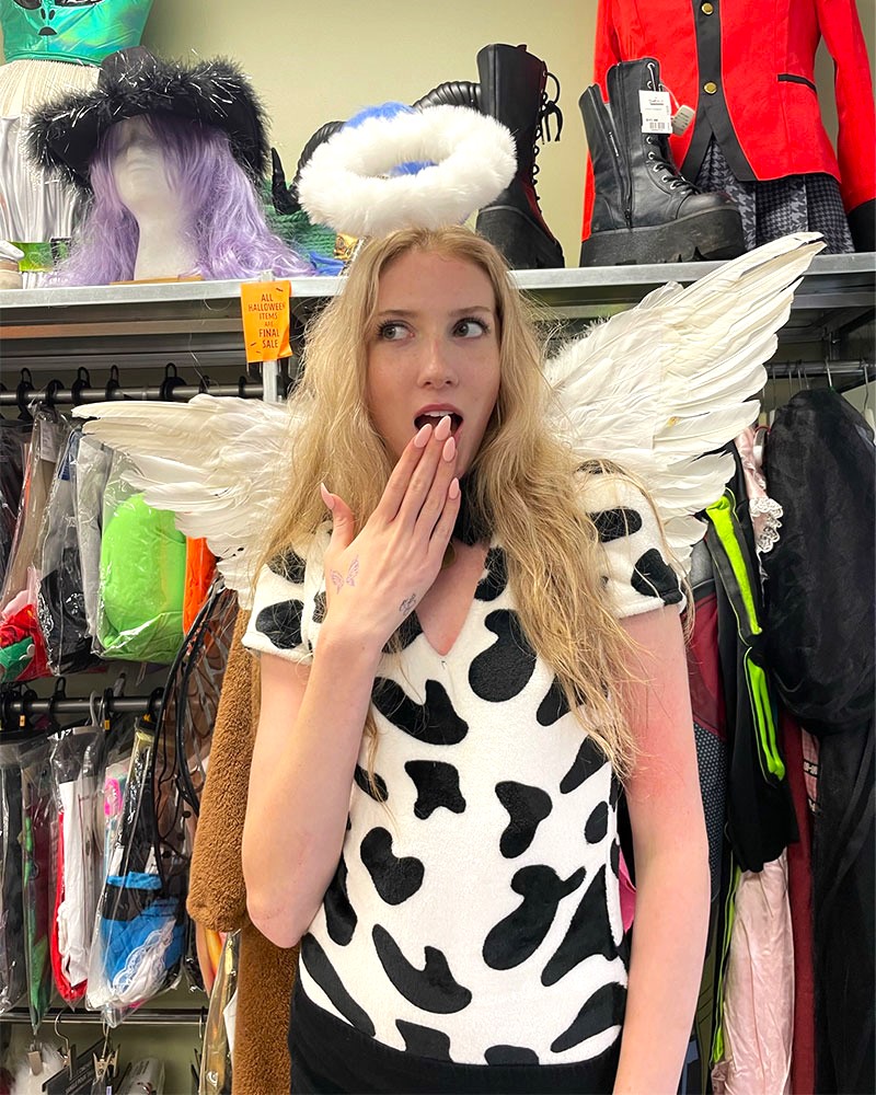 Person wearing cow print tee shirt, angel wings and fuzzy halo headband