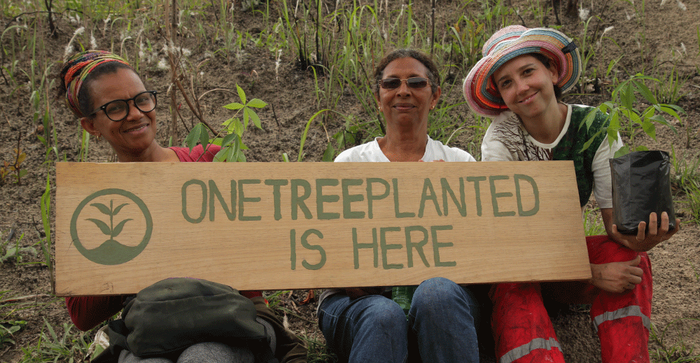 Three volunteers holding sign that reads "One Tree Planted Is Here"