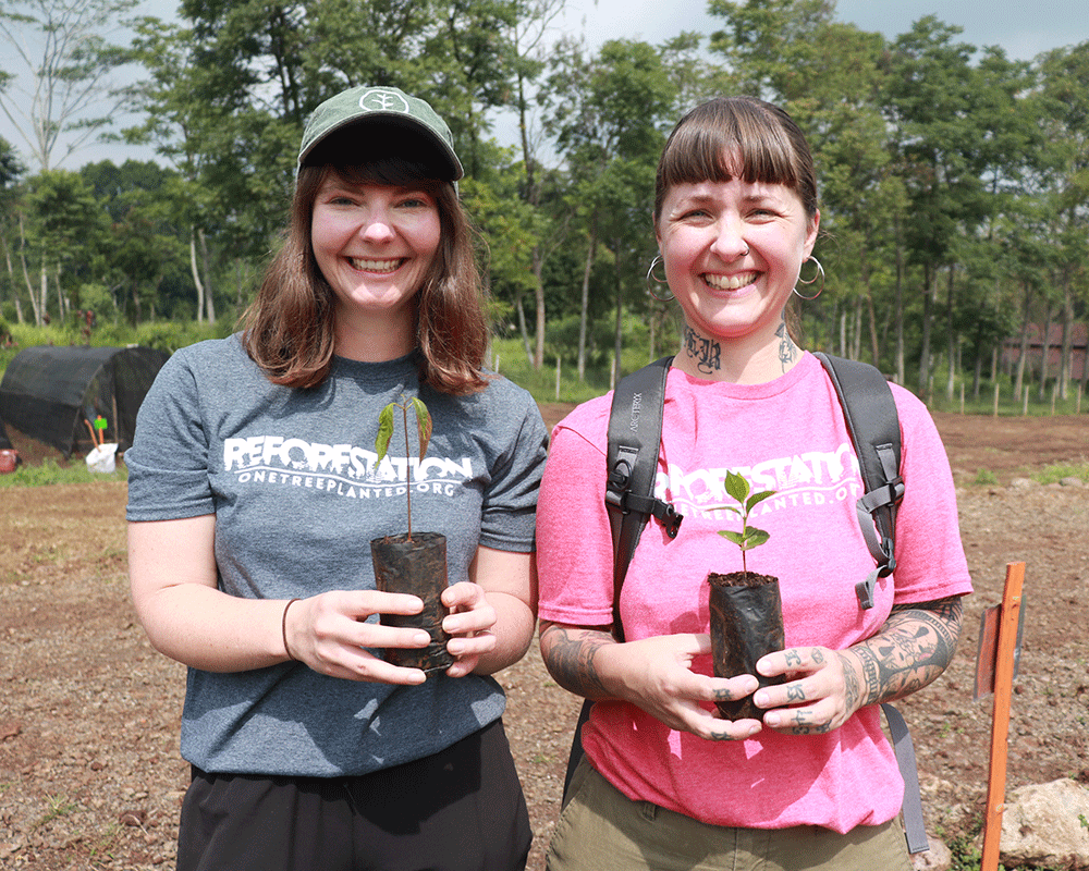 Two volunteers holding small tree saplings