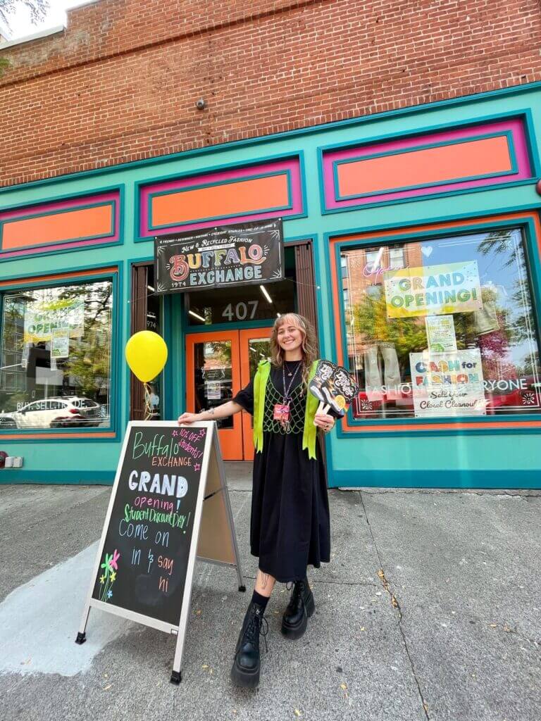 Buffalo Exchange Spokane employee standing outside of store near sign that reads "Grand Opening!"