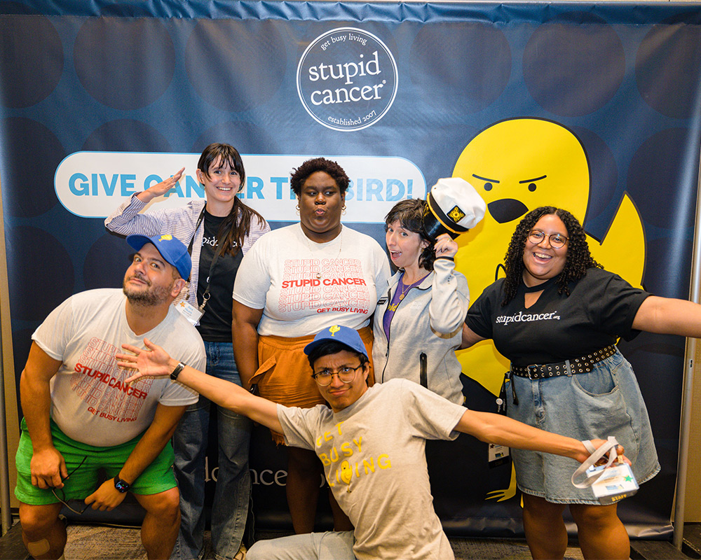 A group of attendees at a Stupid Cancer event. Posing in front of Stupid Cancer banner.
