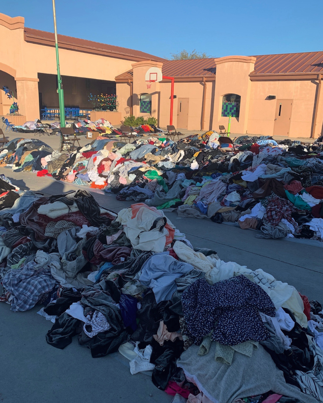 Piles of clothing laid across an elementary school basketball court for a Clothing for the Community $1 sale