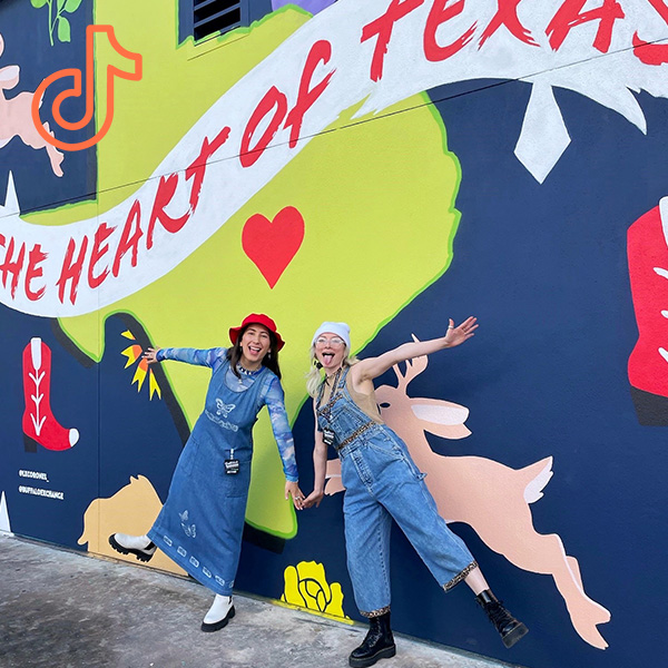2 people wearing denim in front of Heart of Texas Mural