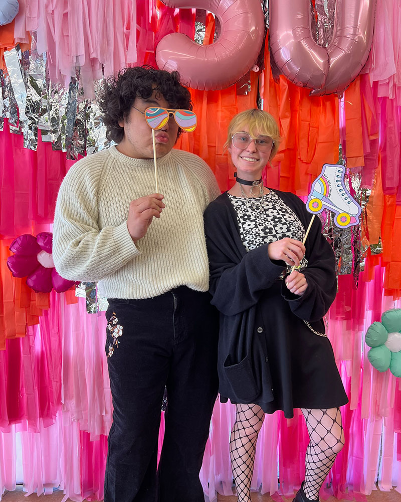 2 people posing with 70s props in front of pink backdrop