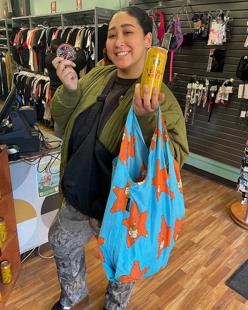 Buffalo Exchange customer posing by counter with shopping bag and holding sticker and canned drink