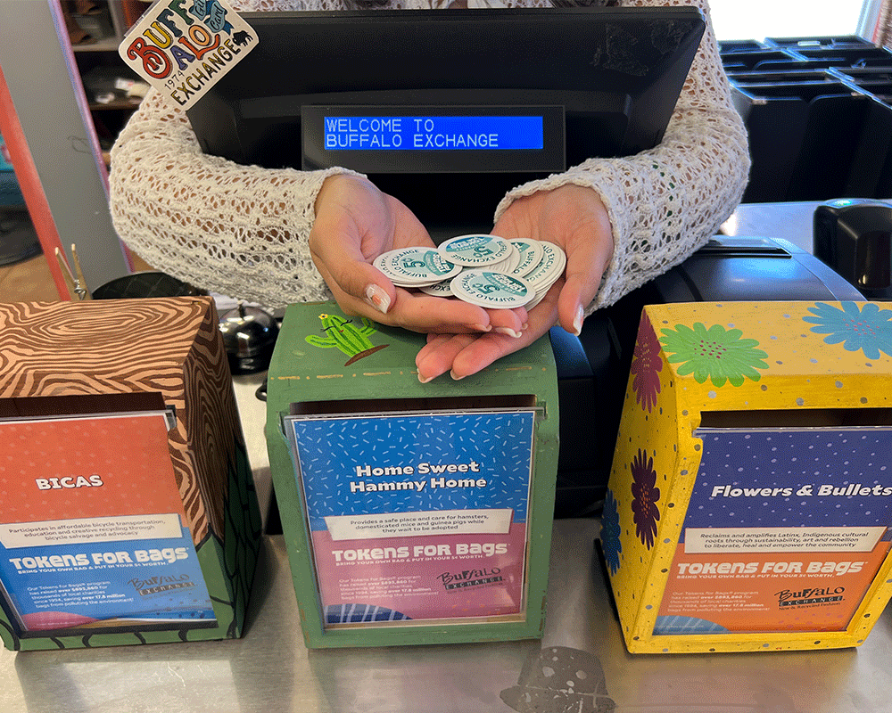 Buffalo Exchange employee holding tokens for tokens for bags program over donation boxes